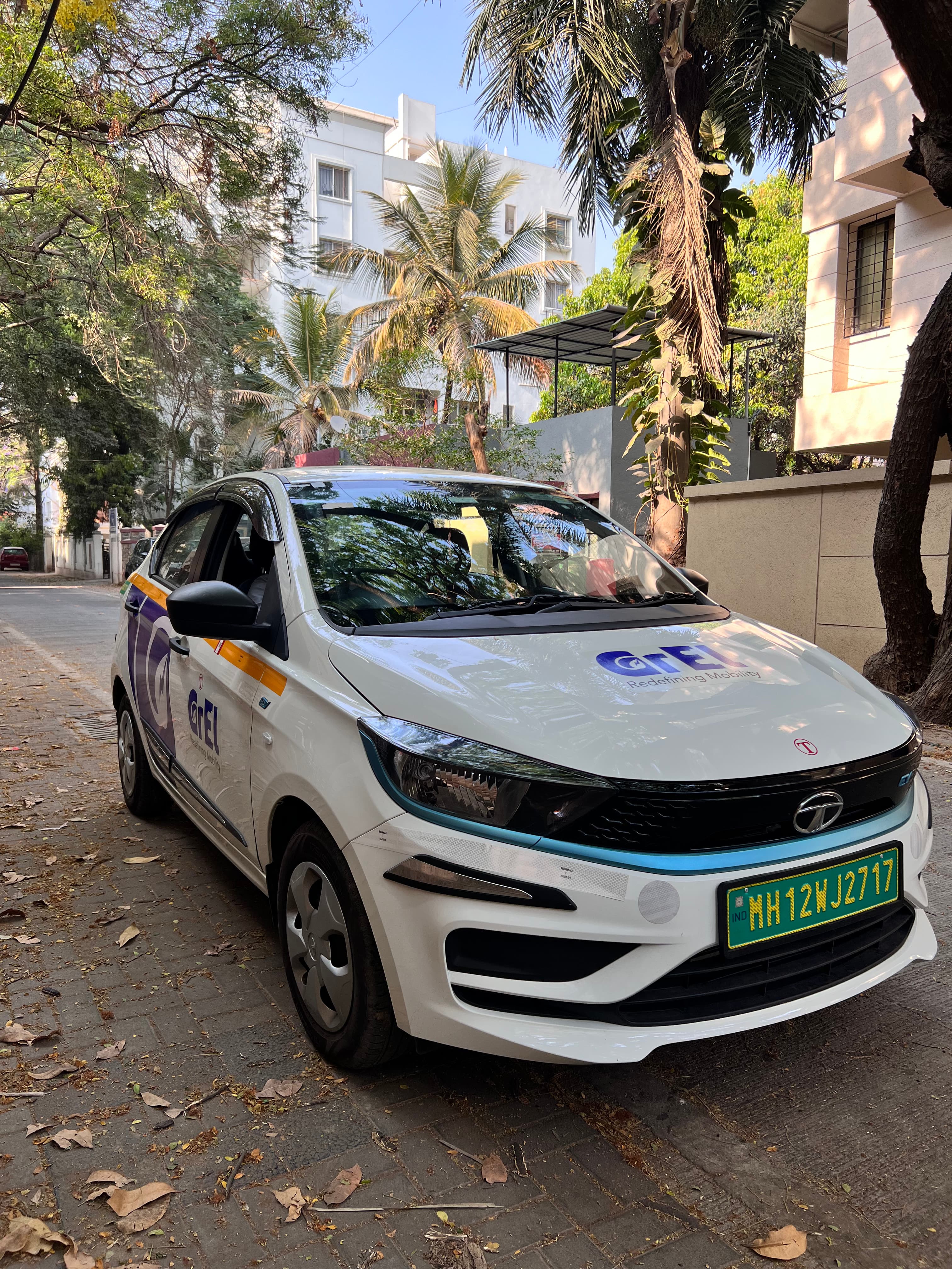 A white GrEL Tata Tigor EV parked on a leafy residential street in Pune